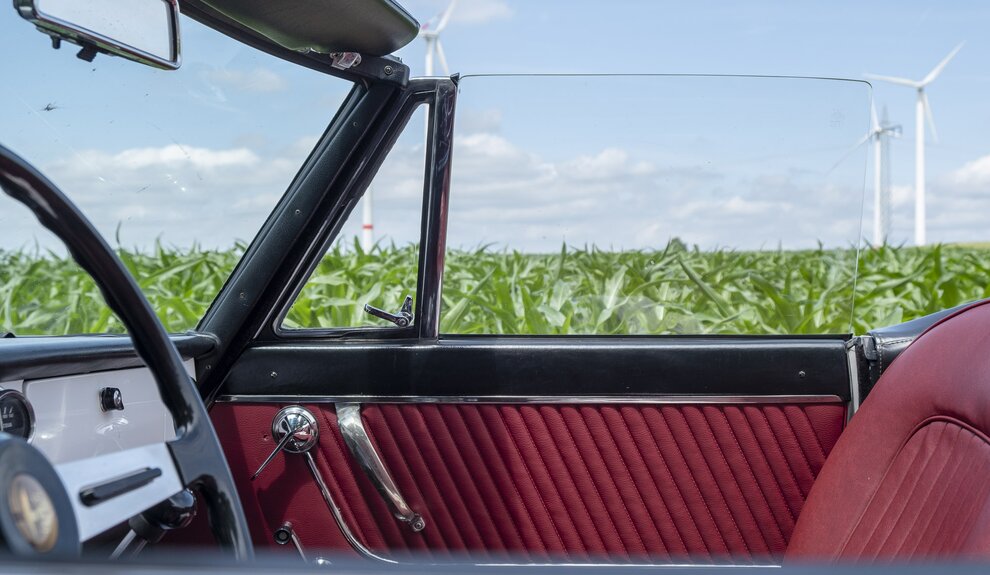 Rote Polsterung und Lenkrad eines Oldtimer Cabriolets vor einer grünen Wiese mit Windrädern. | © Andreas Körner | bildhübsche Fotografie
