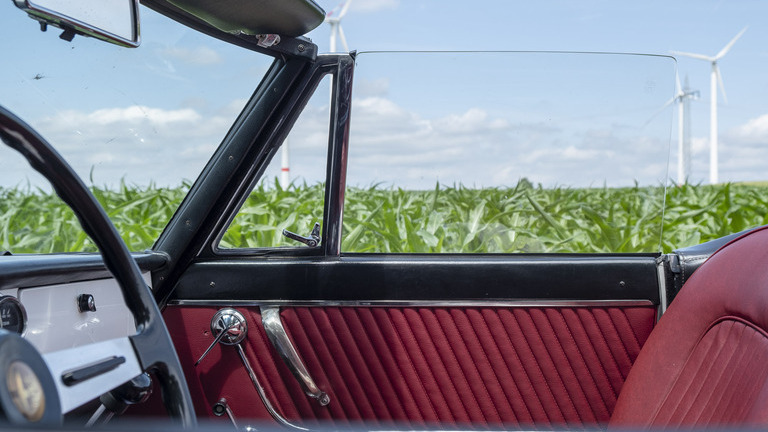 Red upholstery and steering wheel of a vintage convertible in front of a green meadow with windmills. | © Andreas Körner | bildhübsche Fotografie
