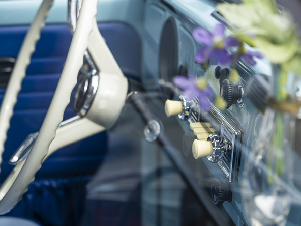 Interior view of a vintage car with a white steering wheel and blue interior trim, as well as a small vase with purple flowers above the radio. | © Andreas Körner | bildhübsche Fotografie