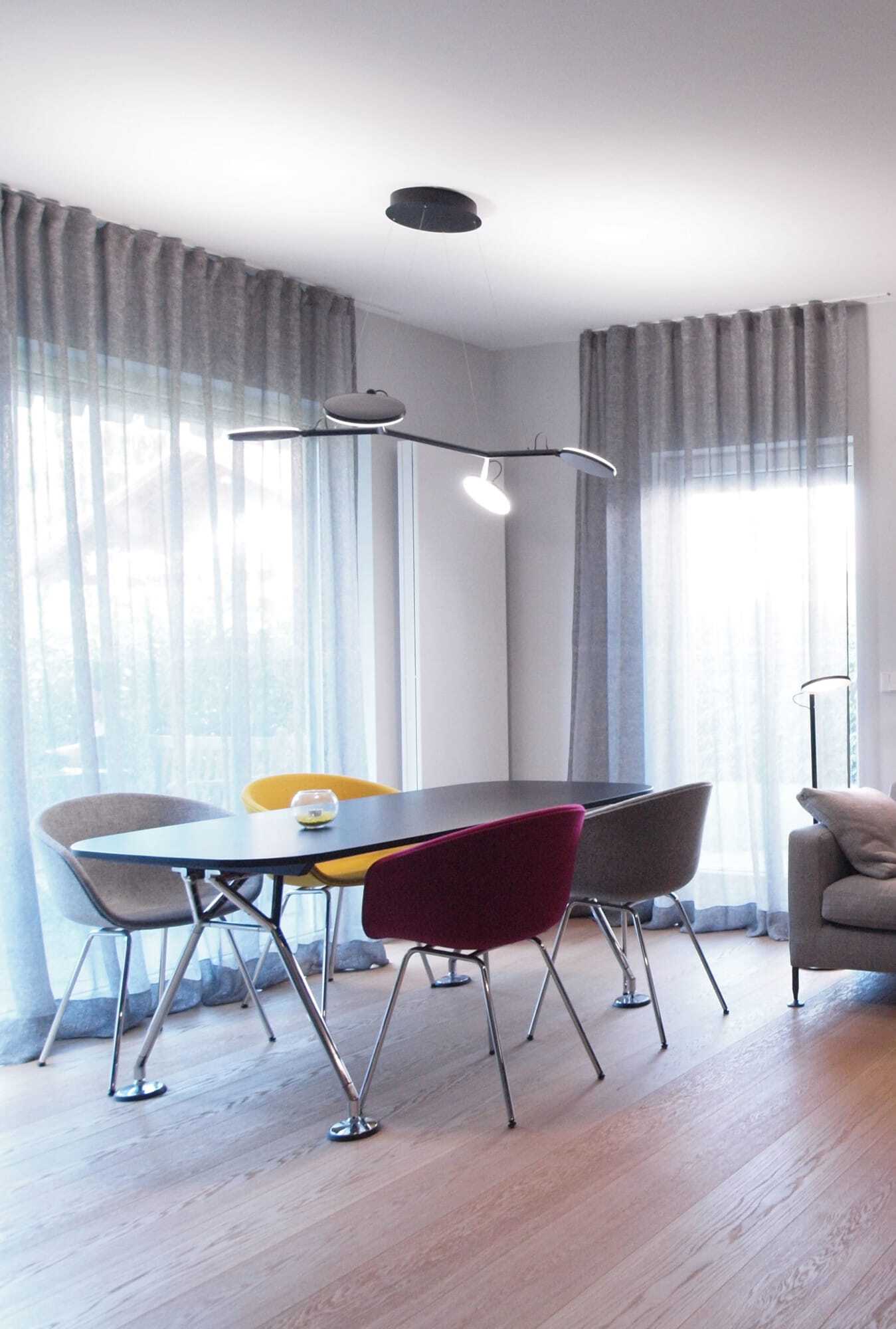 Pendelleuchte mit vier beweglichen Lichtköpfen an einer verzweigten Gehäusestruktur mit Deckenbaldachin über Esszimmertisch und passende Stehleuchte mit einem Kopf neben angeschnittenen grauen Sofa.