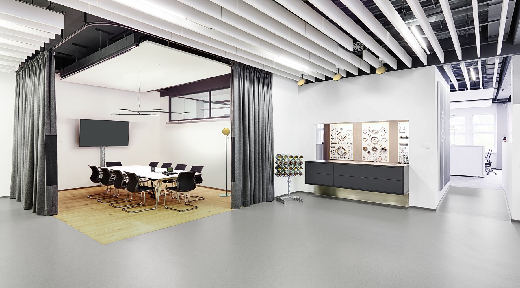 Open office space, in a meeting room separated by curtains hangs a black branched luminaire with round light heads of AVVENI Pendant 5 - Type 3, next to the table stands a floor lamp with a golden round luminaire head.