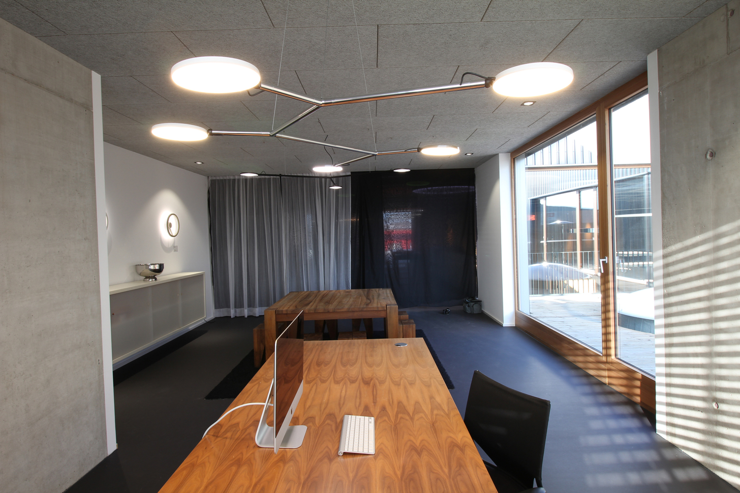 Verzweigte Leuchte aus poliertem Aluminium mit 5 beweglichen flachen, runden Leuchtenköpfen, AVVENI Pendant 5 Typ 3, abgehangen über einem modernen Holz-Bürotisch.