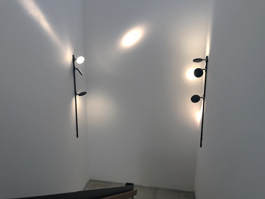 White staircase, with two black surface-mounted track systems lightlight + 2 flexible AVVENI luminaire heads, left and right at the height of the staircase turning platform.
