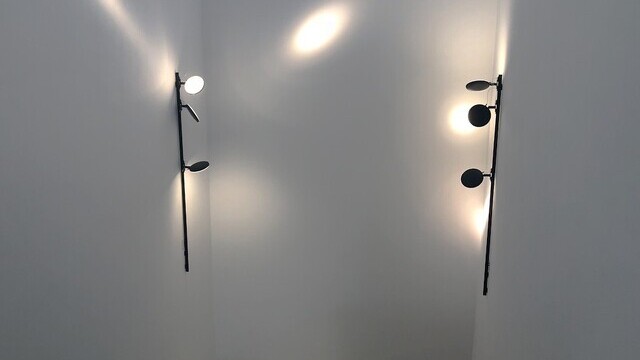 Weißes Treppenhaus, mit zwei schwarzen Wandanbau Stromschienensystemen lightlight + 2 flexiblen Leuchtenköpfen AVVENI, links und rechts auf Höhe des Treppen-Wendepodest.