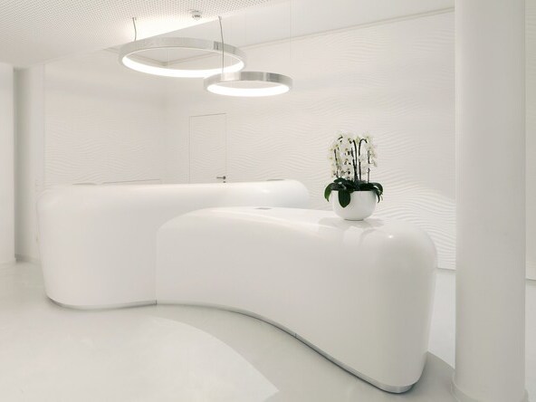 White room with two white futuristic reception counters with orchids on one, 2 aluminium ring lights CIRCOLO are suspended above the counters. | ©  johannes seyerlein seyerleinundseyerlein.de