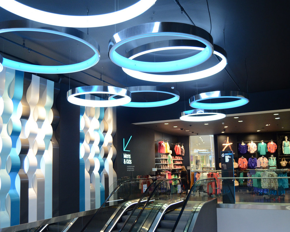 LED-Technik: weiß, tunable & RGB (auch in Kombination) Rolltreppen einer Shopping Mall mit dem Fokus auf darüber abgehangenen Ringleuchten (CIRCOLO L) mit schwarzem Profil und weißer und hellblauer Lichtabstrahlung.