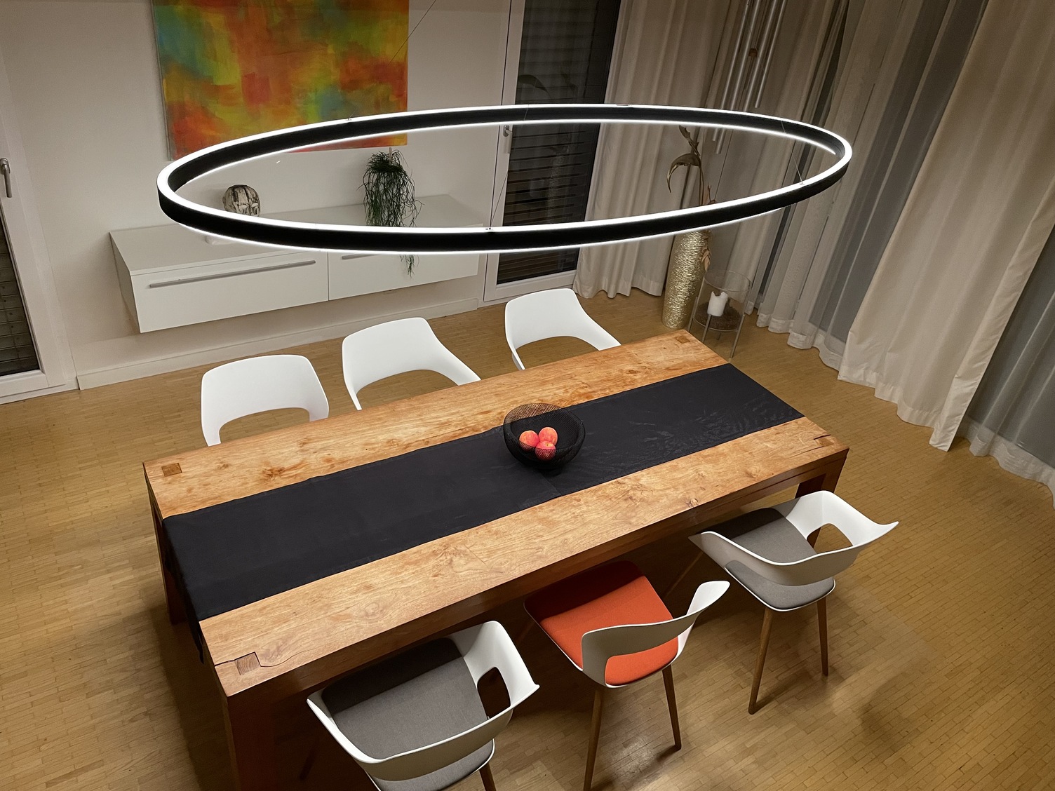 Elliptical ring light Doppio Ellipse provides direct and indirect lighting above a modern wooden dining table.