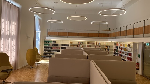 Library of the Technical University of Darmstadt with bookshelves on the wall, acoustic benches in the centre of the room, several DUETTO ring luminaires suspended from the ceiling, some with acoustically effective fabric in the centre of the luminaires.