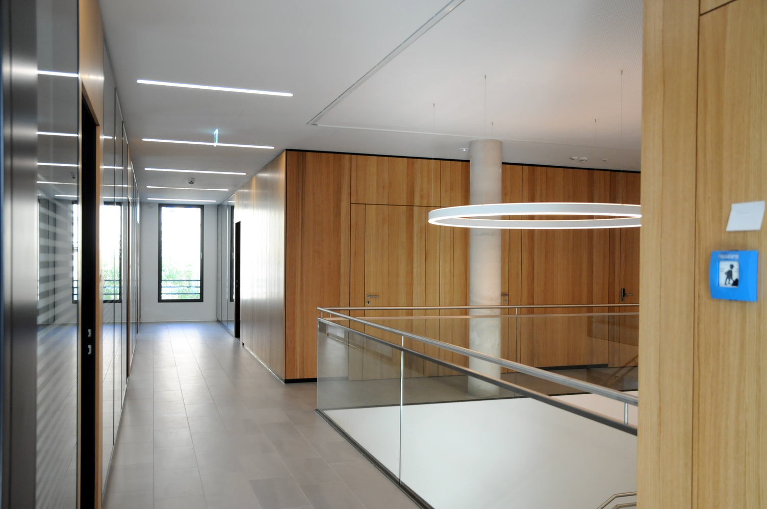 Corridor in a modern office building, on the right in the picture a white ring light (DUETTO direct/indirect 1924 mm).