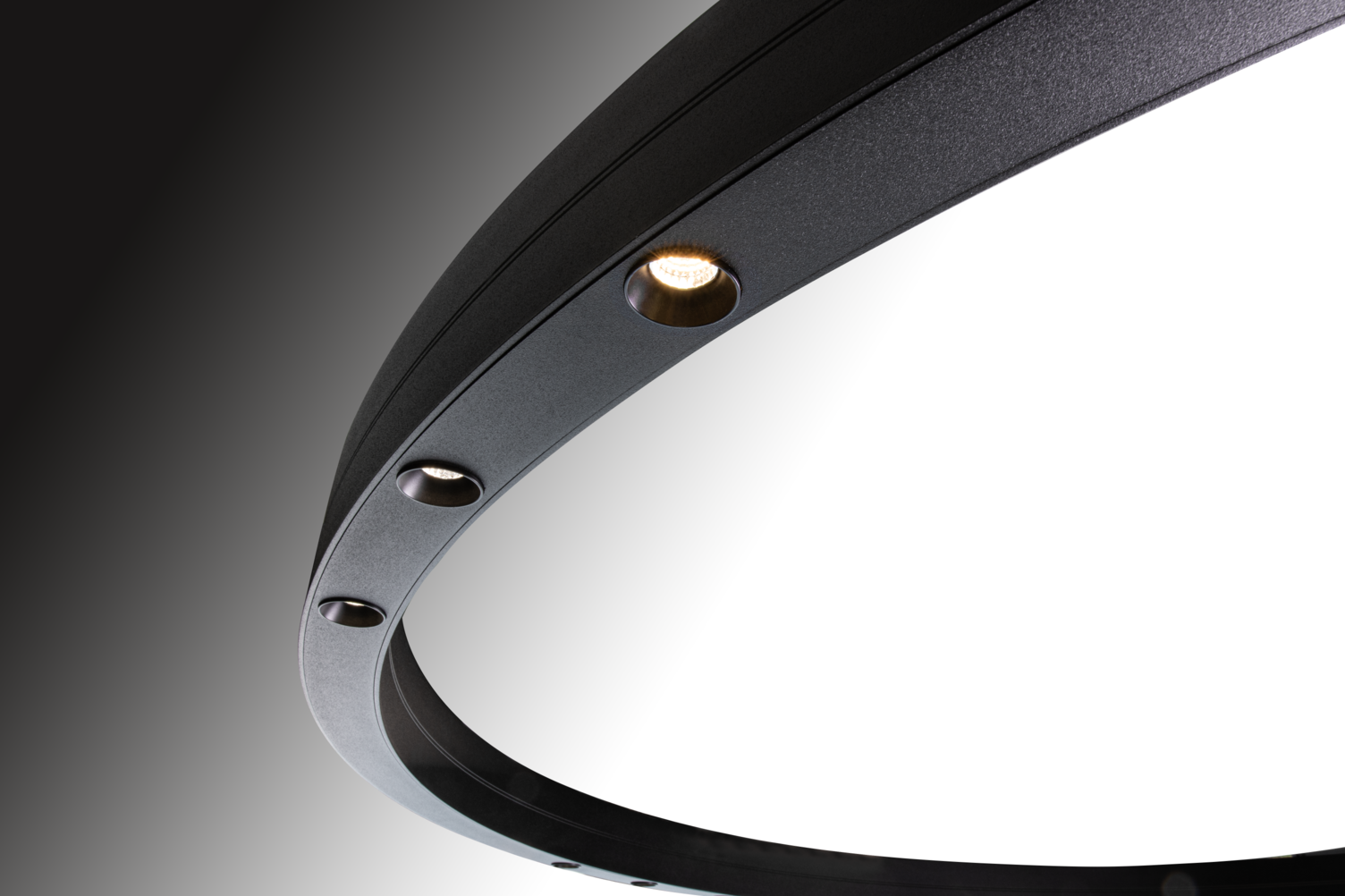 Ausschnitt einer schwarzen Ringleuchte, DUETTO LENS, sichtbar sind drei runde leuchtende Linsen mittig im Ringprofil direkt leuchtend.