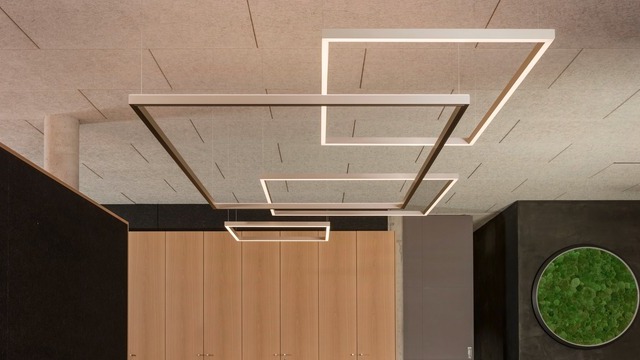 Four square LED frame lights (GIOCO) with direct and indirect lighting in an elegant finish, suspended in various sizes and heights from a light spaghetti ceiling in front of a wooden wall, with a black wall and a green round moss light in the background on the right. | © bildhuebsche Fotografie - Andreas koerner
