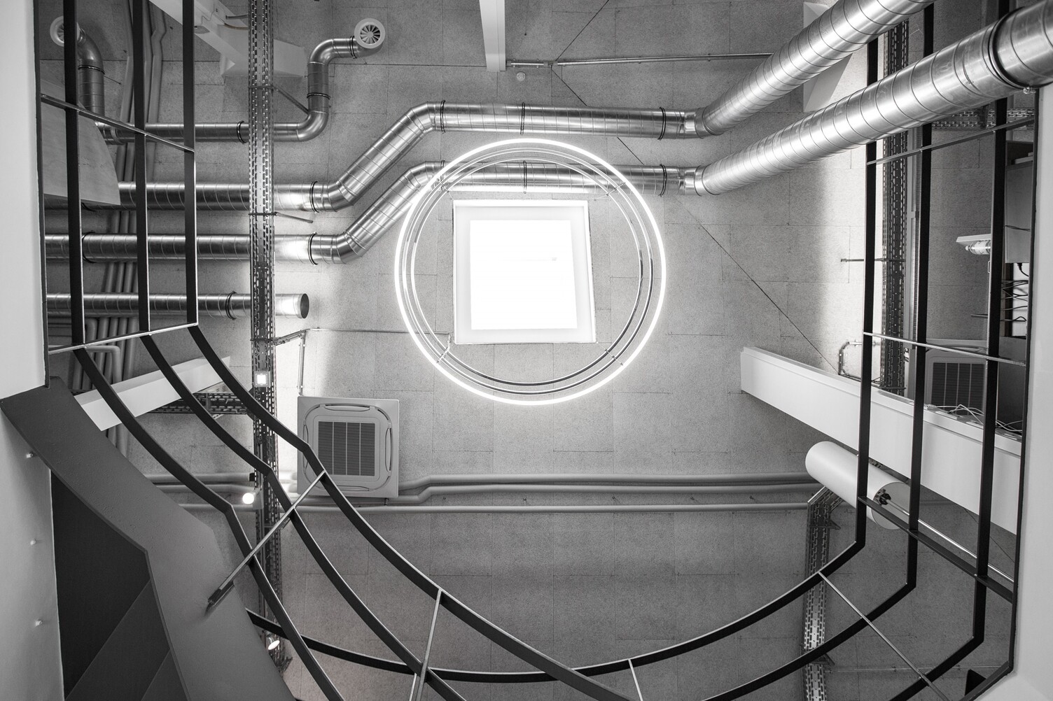 View from below in a stairwell of a concrete industrial building of madness GmbH to the ceiling of 3 INSIEME ring lights suspended one below the other.