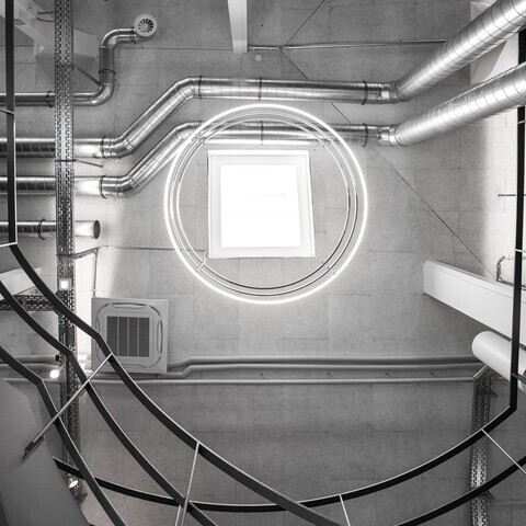 View from below in a stairwell of a concrete industrial building of madness GmbH to the ceiling of 3 INSIEME ring lights suspended one below the other.