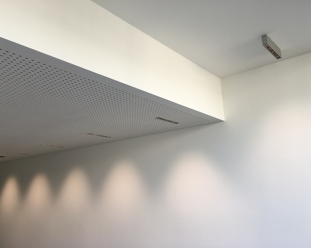 Corridor lighting with PALADIO linear recessed and surface-mounted downlights Corridor with a stepped ceiling. Linear recessed PALADIO downlights are fitted into the lower perforated ceiling. A linear surface-mounted PALADIO downlight is visible in the recessed ceiling.