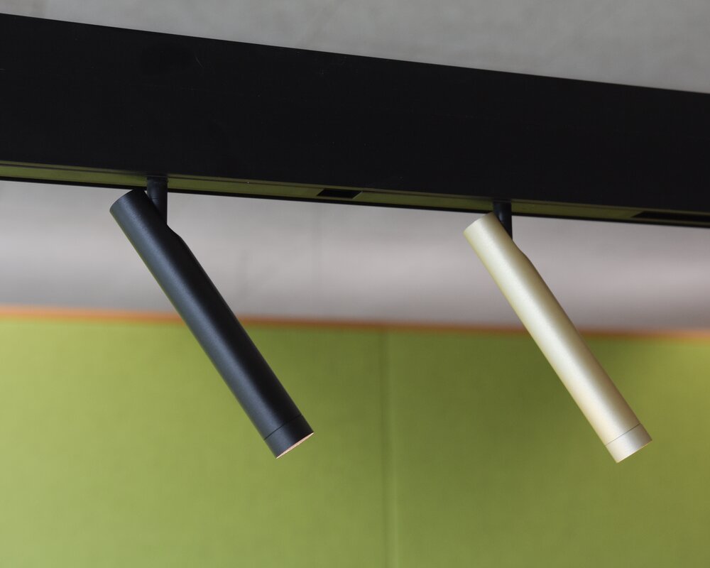 Beweglicher schmaler zylindrischer FINO SPOT 2 als Lichtelement für PALADIO TRACK | © SATTLER Vor einer grünen Filz-Wand: Ausschnitt einer schwarzen linearen Stromschienenleuchte PALADIO TRACK mit zwei eingesetzten beweglichen,schmalen zylindrischen Spots (FINO SPOT 2) in schwarz und Champagner-Gold, die schräg nach rechts vorne leuchten. | © SATTLER