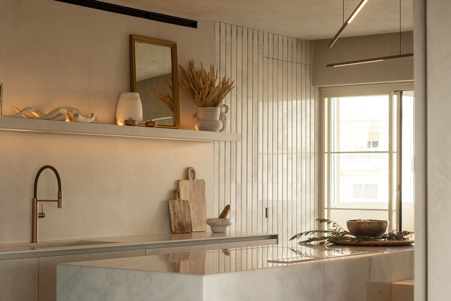 Kitchen lighting. Mediterranean kitchen with light marble kitchen block above, two cylindrical PALITO pendant lights in bronze hanging above. Horizontal alignment of the lights, which shine downwards in a linear fashion on one side of the light fixture.