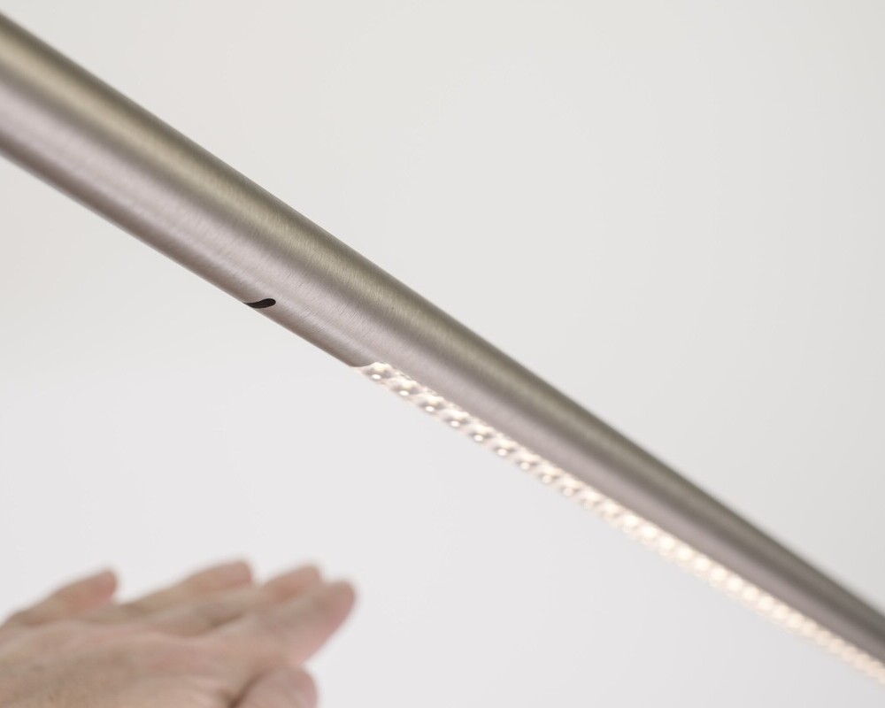 Gestensteuerung | © Andreas Körner | bildhübsche fotografie Zylindrische schräg horizontal verlaufende Aluminiumleuchte, unter einem kleinen Rohrloch ist eine Hand zu sehen, im weiteren Verlauf der zylindrischen Leuchte sind im Bild rechts leuchtende Linsen zu sehen. Bild stellt im gesamten die Gestensteuerung wie Dimmung der Leuchte dar. | © Andreas Körner | bildhübsche fotografie