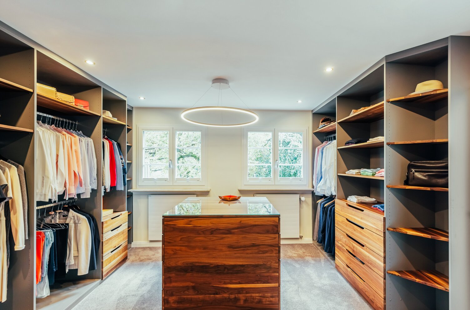 Ankleidezimmer mit Ringpendelleuchte SLIM DIRECT | © Frank Luger Moderner Ankleideraum mit links und rechts vom Raum Regalen und Schränken mit Kleidung in der Mitte ein Holz-Tischblock über dem eine Ringleuchte SLIM DIRECT hängt. | © Frank Luger