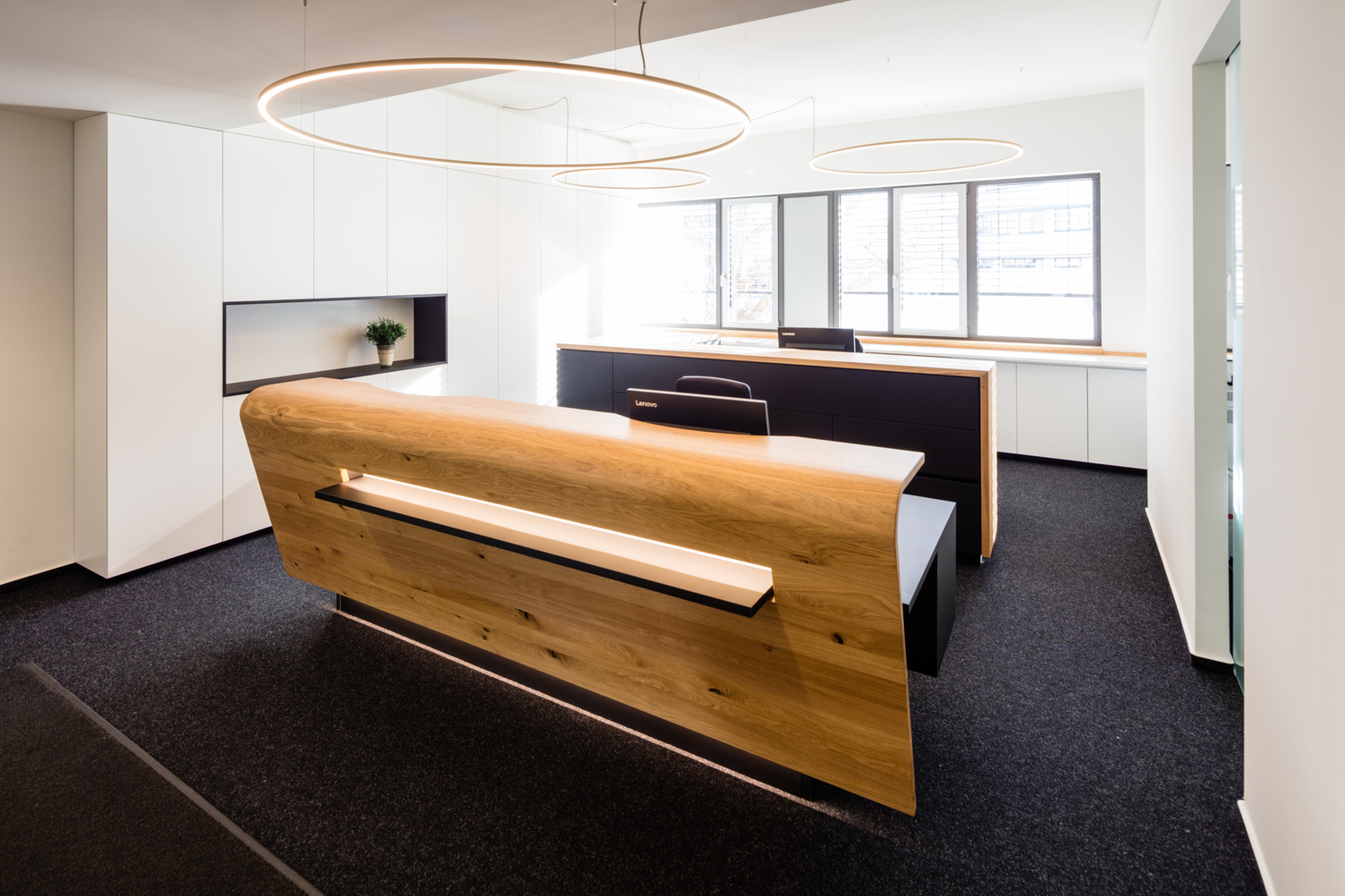 Wooden reception desk of a notary's office with three ring lights (SLIM) of different sizes suspended above it.