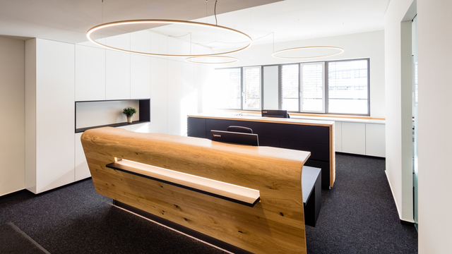 Wooden reception desk of a notary's office with three ring lights (SLIM) of different sizes suspended above it.