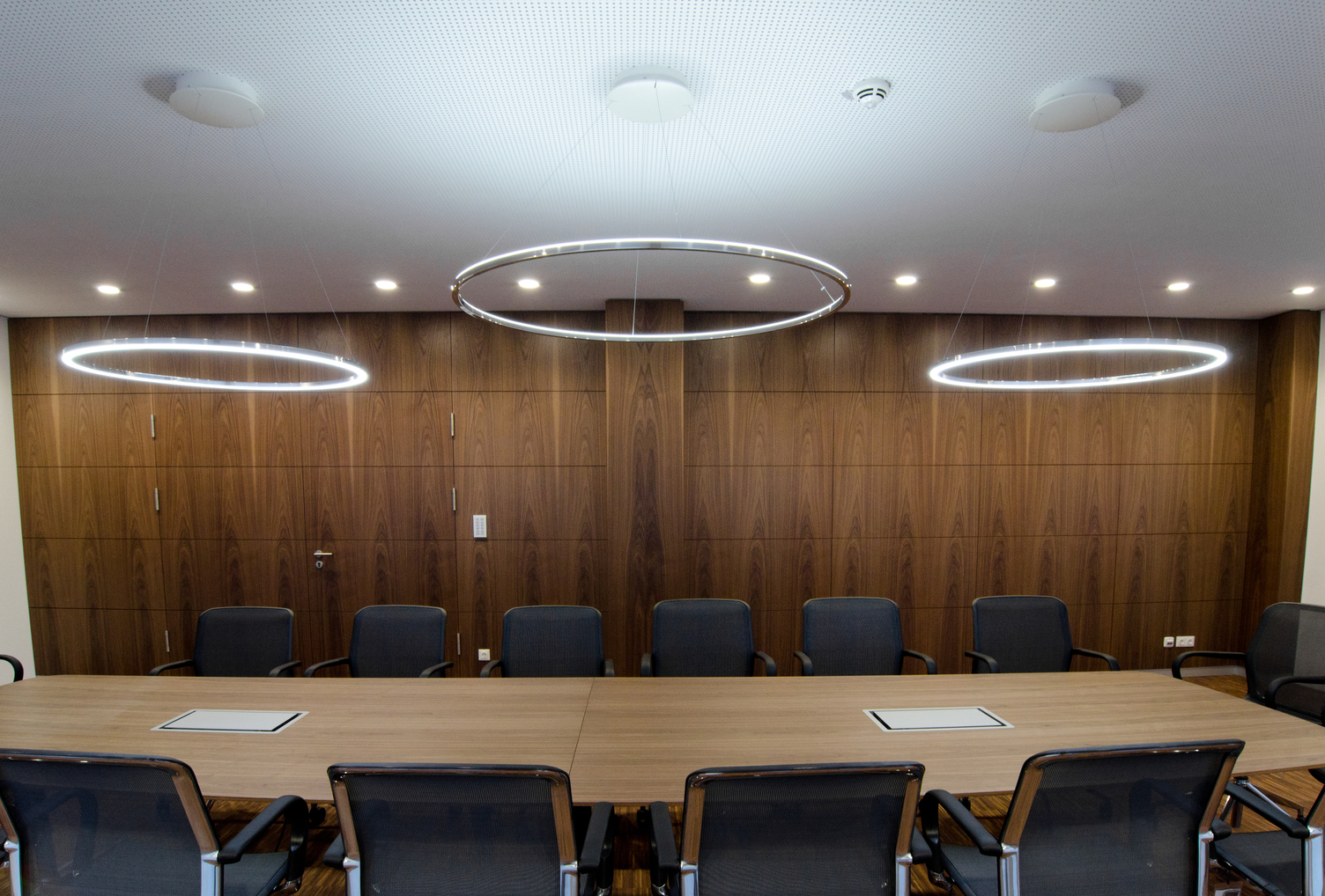 Three SLIM Ring Lights in Polished Aluminium above Conference Table – Direct & Indirect Combined Three SLIM LED ring luminaires by SATTLER in polished aluminium above a conference table, two outer rings emitting direct light and one central ring providing indirect illumination.