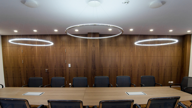 Three SLIM LED ring luminaires by SATTLER in polished aluminium above a conference table, two outer rings emitting direct light and one central ring providing indirect illumination. | © Horst Mohring