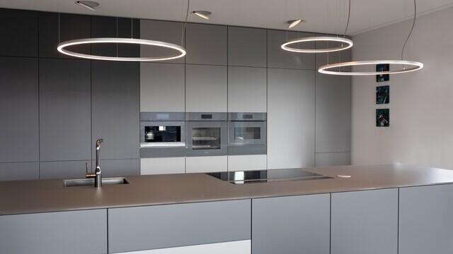 Three filigree SLIM DIRECT LED ring luminaires by SATTLER in brushed aluminium above a kitchen counter, providing direct lighting for a modern private kitchen.