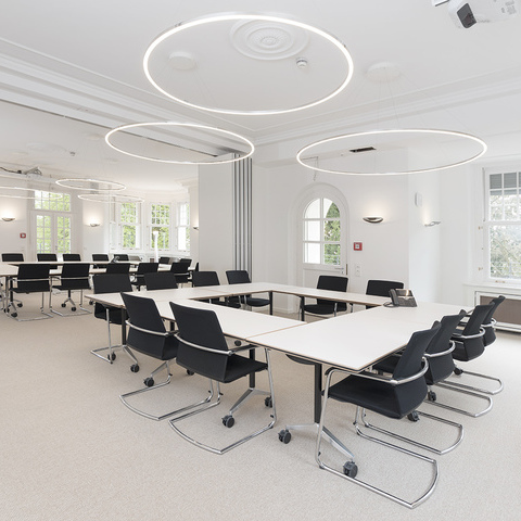 Heller Seminarraum der Lohmann & Rauscher Academy mit SLIM Ring-Leuchten von SATTLER. Flexible Tischanordnung für Schulungen und Workshops.