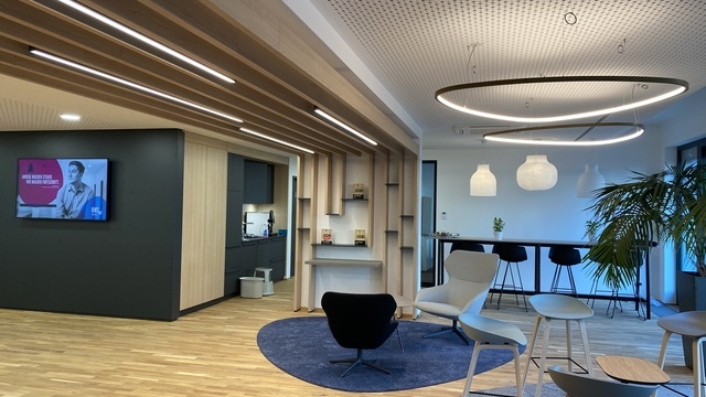 Two SLIM DELTA LED ring luminaires and several PALADIO pendant lights by SATTLER above a lounge area, filigree ring lights combined with slatted pendants for balanced ambient lighting.