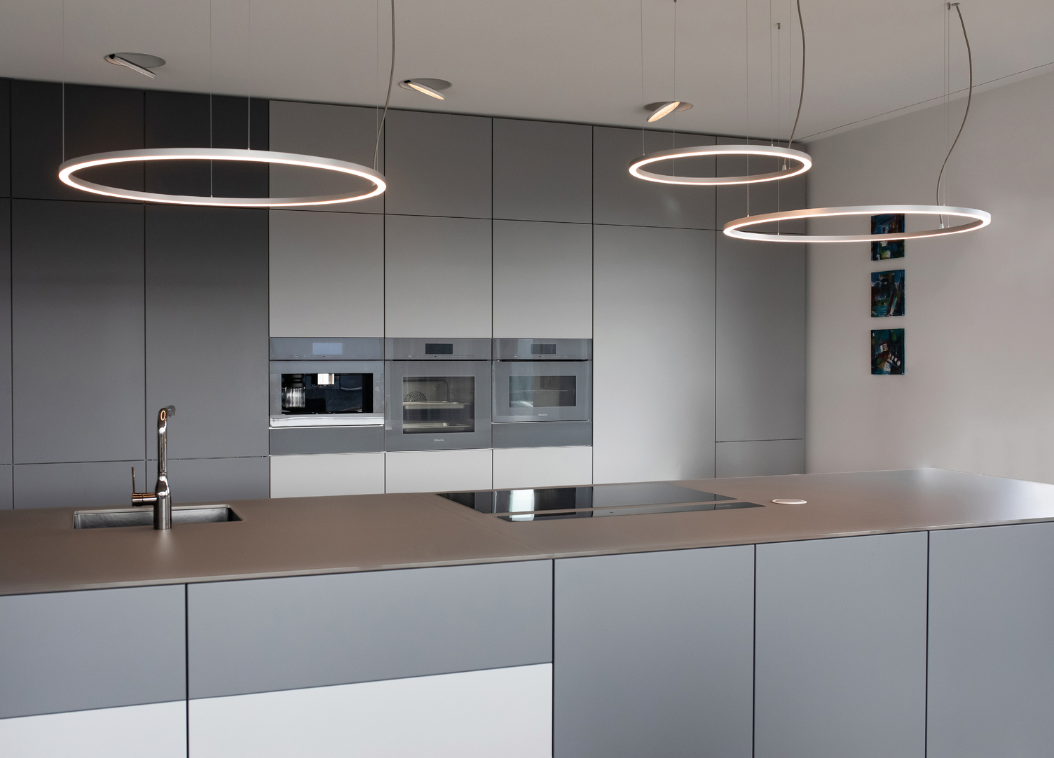 Modern light grey open kitchen 3 small SLIM DIRECT ring lights hang side by side above the kitchen unit, offset in height.