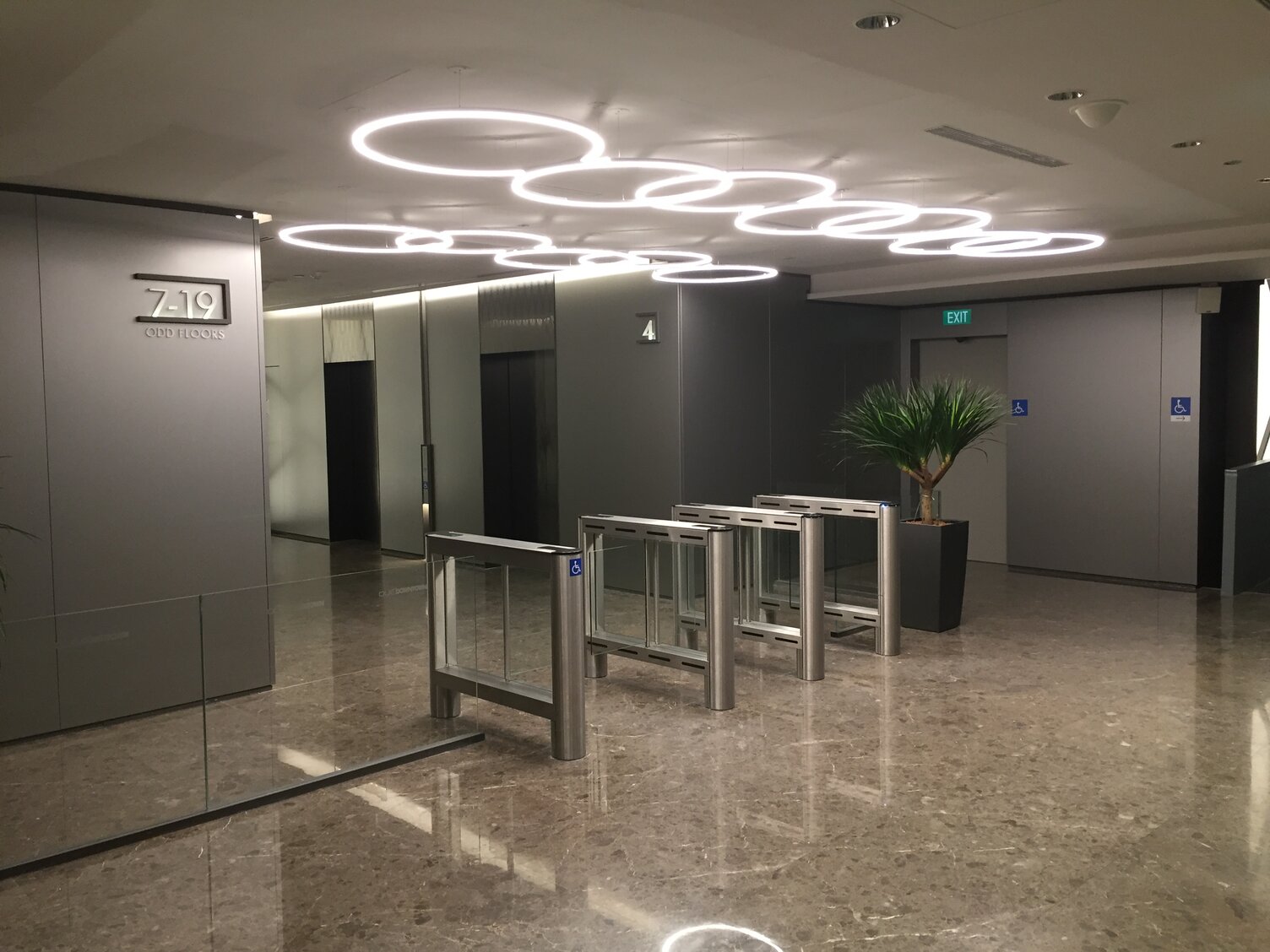 Fokusierung Sicherheitsdurchgang Büro mit SLIM Ringleuchten Sicherheitsschranken in einem Bürogebäude OUE Downtown, Singapur. Über den Schranken Anordnung von zwei parallelen Reihen mehrerer überlappend abgehangenen SATTLER SLIM Ringleuchten.