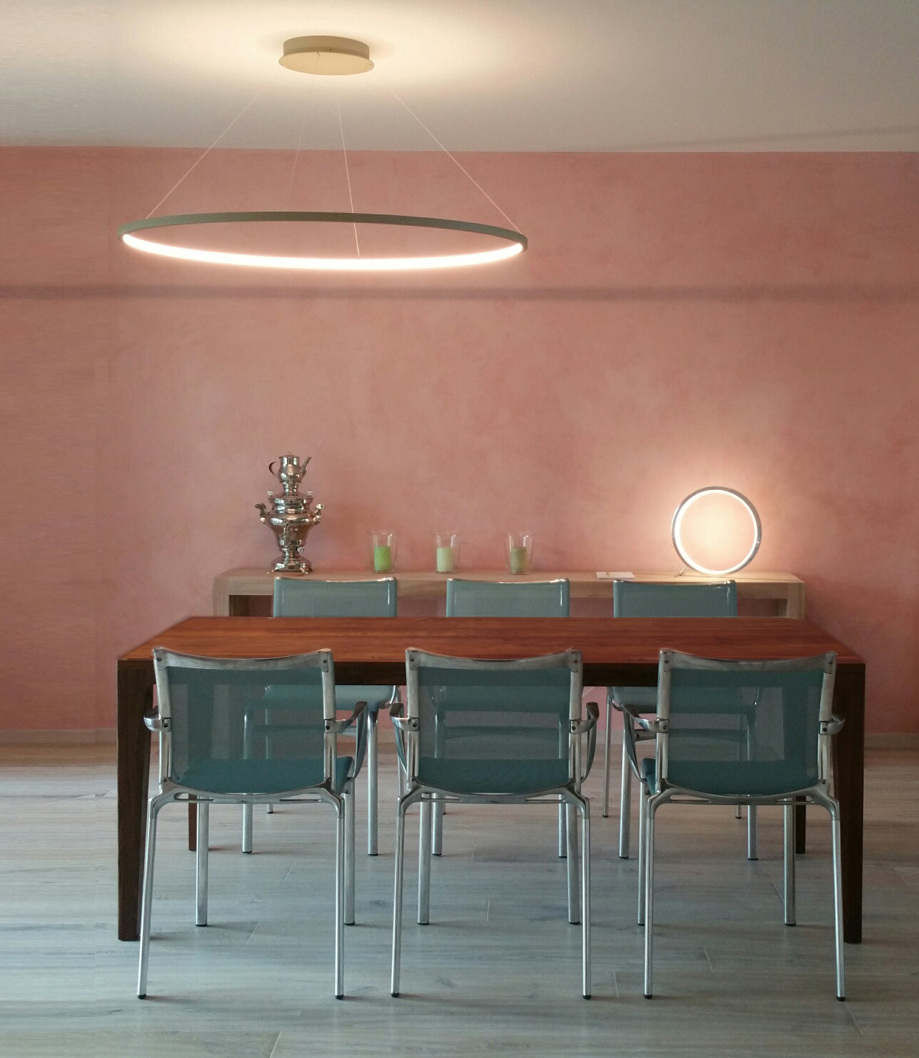 Rosa gestrichenes Esszimmer mit weißer Ringpendelleuchte Slim in über braunem Esstisch mit grünen Stühlen. Im Hintergrund auf Seitenanrichte runde Ringtischleuchte Slim Table in Aluminium poliert nach innen strahlend