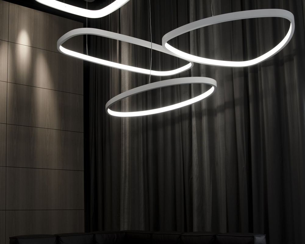 SOFT series pendant light shapes - square, rectangle, triangle, ellipse Shows large SOFT series pendant light shapes from SATTLER with white profile in front of wooden wall with the shapes with rounded corners: square = SOFT QUADRA (here with L-diffuser), all others with I-diffuser: rectangle (SOFT SQUARE), triangle (SOFT DELTA), ellipse.