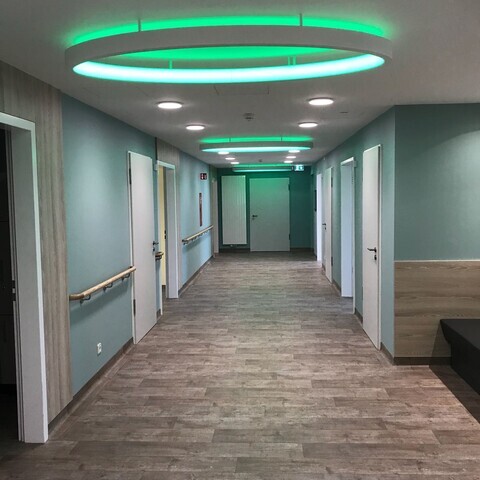 Flur der Paracelsus Klinik zum Kreisssaal mit grünen Wänden und vielen Türen, an der Decke sind elliptische große Ringleuchten durch Distanzhülsen angebracht, die in RGB grün leuchten.