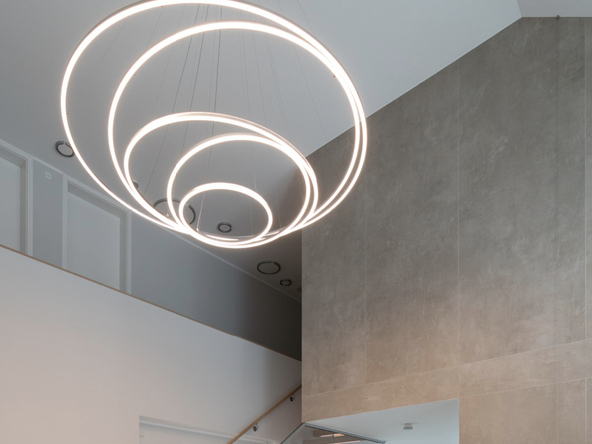 Eingangsbereich mit Treppenhaus mit gerader einläufiger Treppe eines modernen Privathauses und Fokus auf die dekorative Beleuchtung dank eines modernen Kronleuchters bestehend aus 3 Ringleuchten TOCCATA.  | © Luminarium