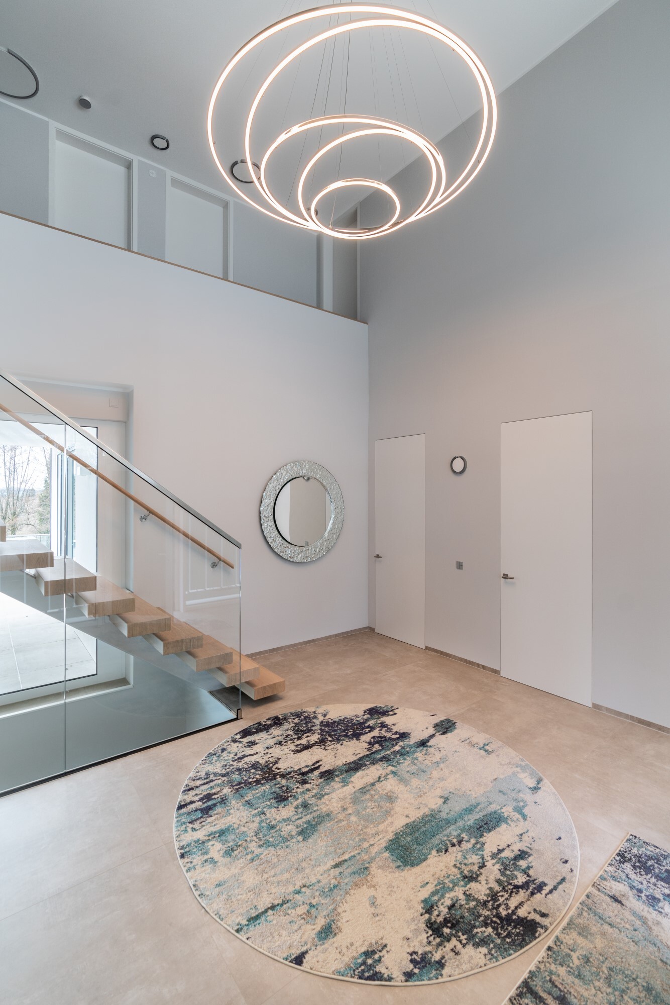 Entrance area with staircase with straight single-flight staircase of a modern private house and focus on decorative lighting thanks to a modern chandelier consisting of 3 TOCCATA ring luminaires.