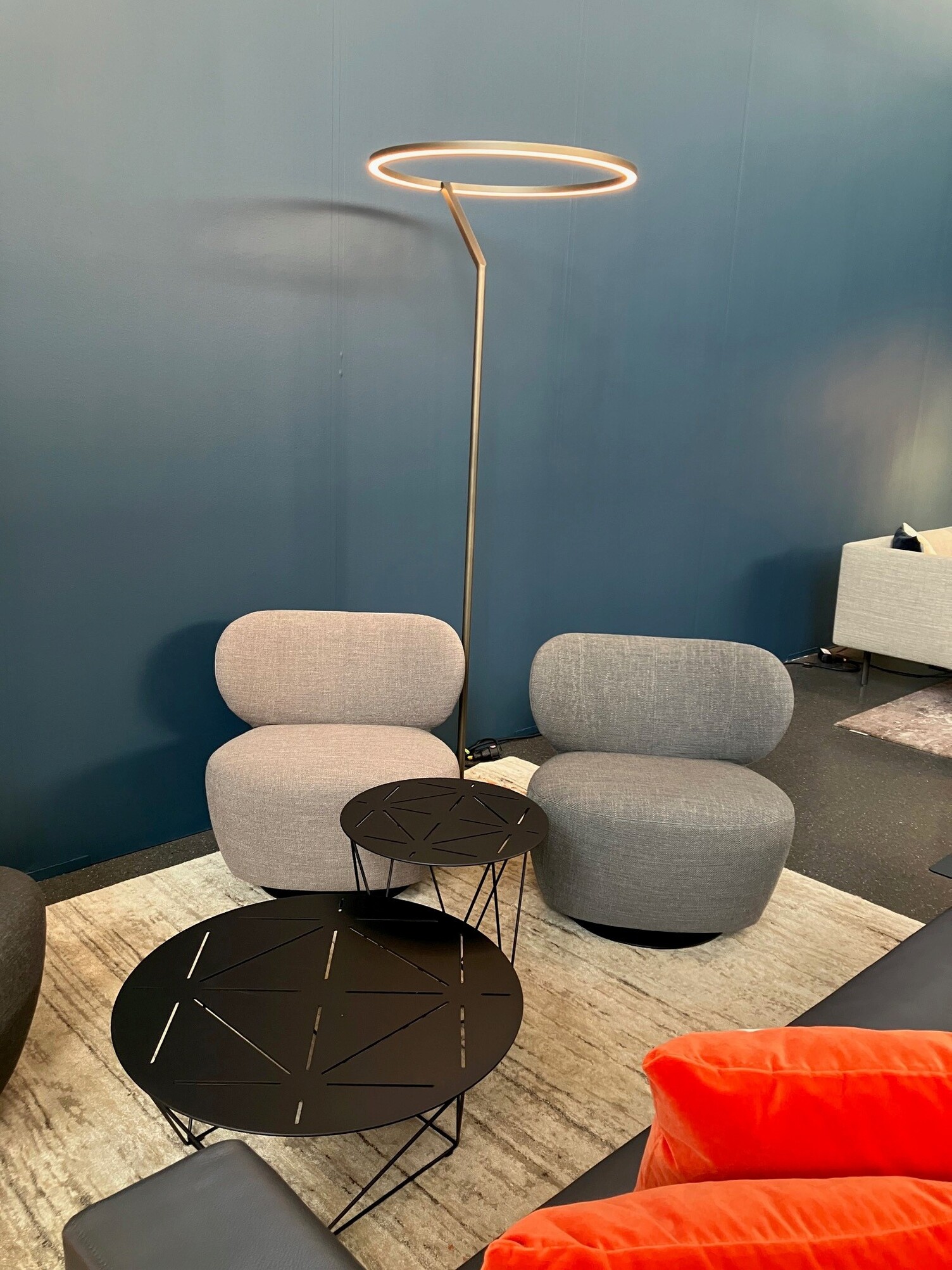 Lounge setting: two grey upholstered armchairs by Walter Knoll against a blue wall, with a large floor lamp – the Insospeso Floor – standing between them, casting a circle of light at the top.