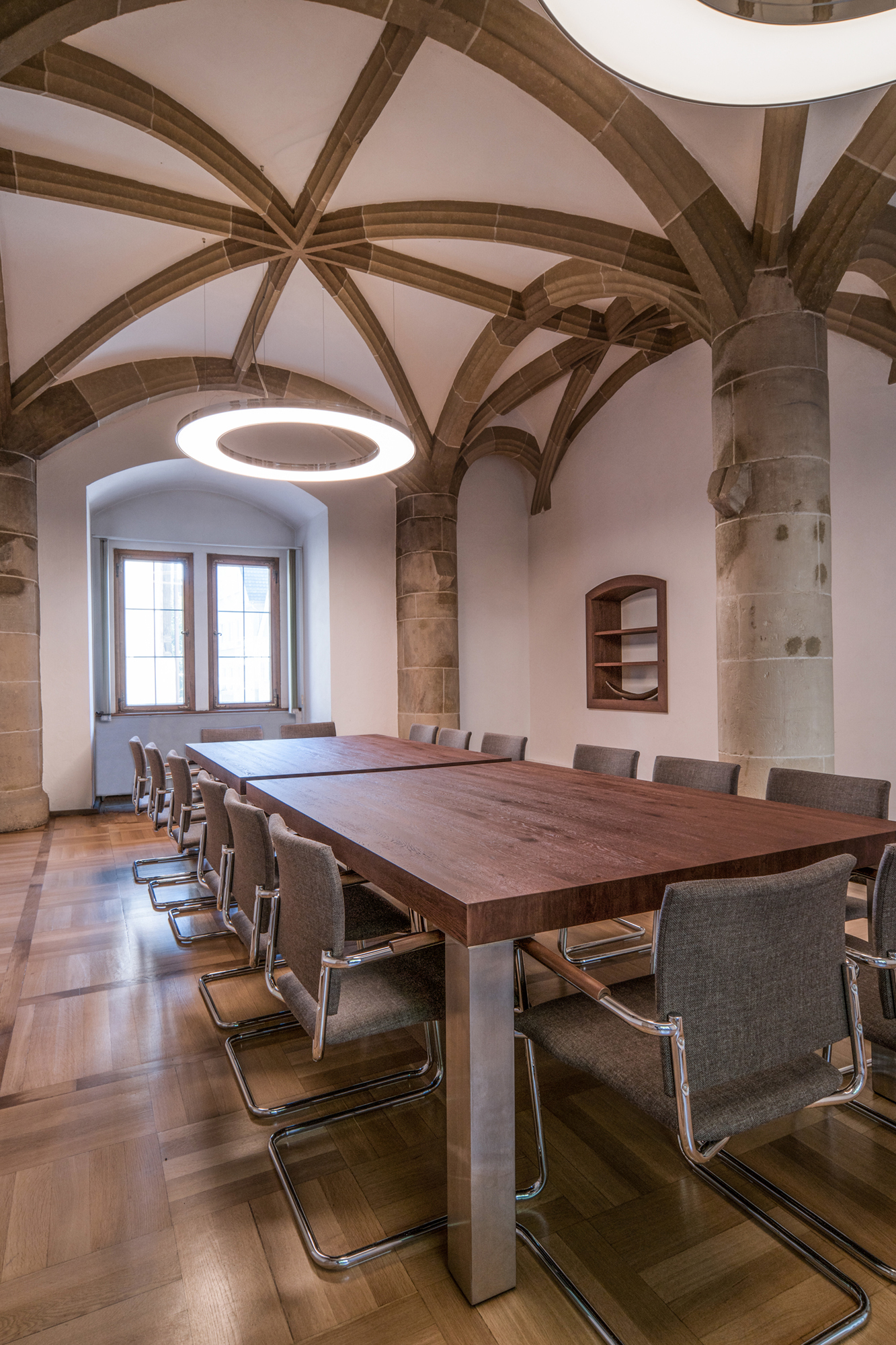 Elegantes Aluminium poliert der Ringleuchten ANELLO passend in historischer Gewölbedecke, weiße Decke und hell steinerne Bögen, über dem großen Besprechungsraumtisch des Amtsgerichts Göppingen. | © SATTLER