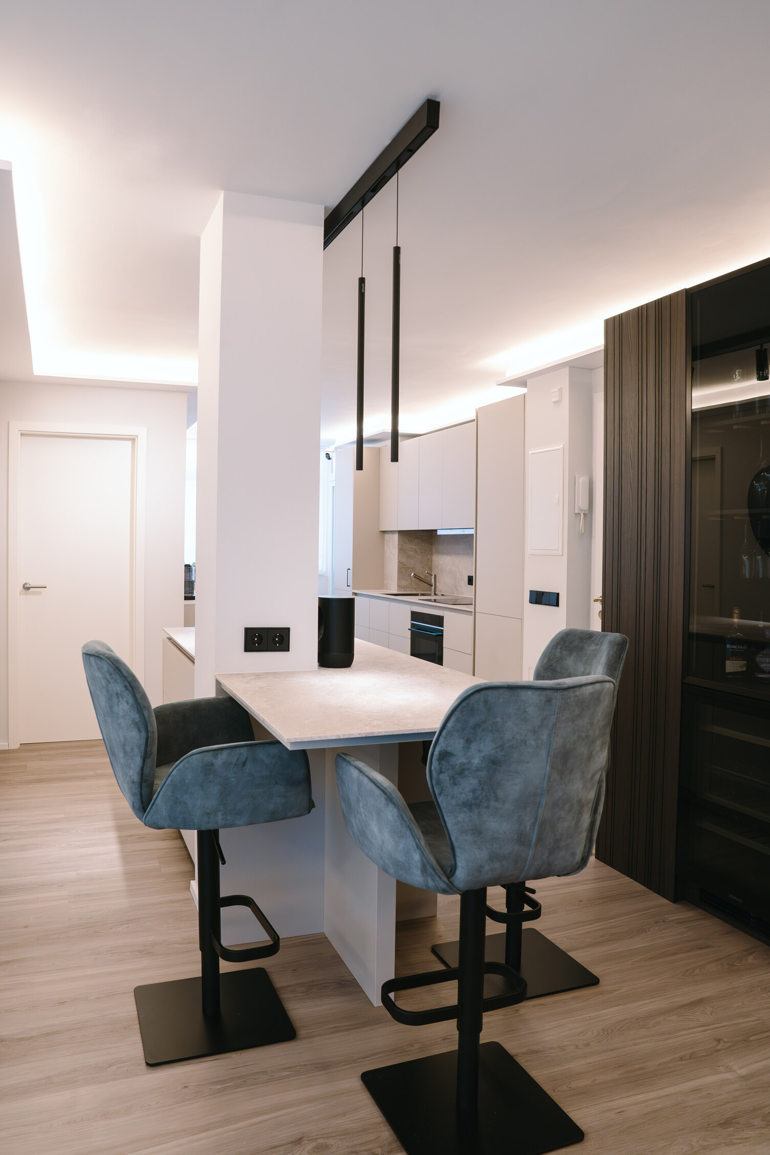 Kitchen high table with blue armchair stools around it, surrounded by cylindrical pendant lights, FINO PENDANT, suspended from a linear element, PALADIO TRACK.