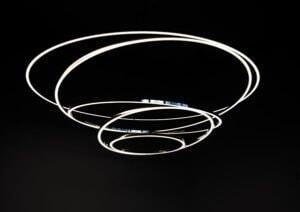 Schwarzer Hintergrund auf dem die TOCCATA Ringleuchte aus 5 schmalen Aluminium-Ringprofilen, die größte oben, die kleinste unten sind immer an einer Stelle miteinander verbunden, zu sehen ist.