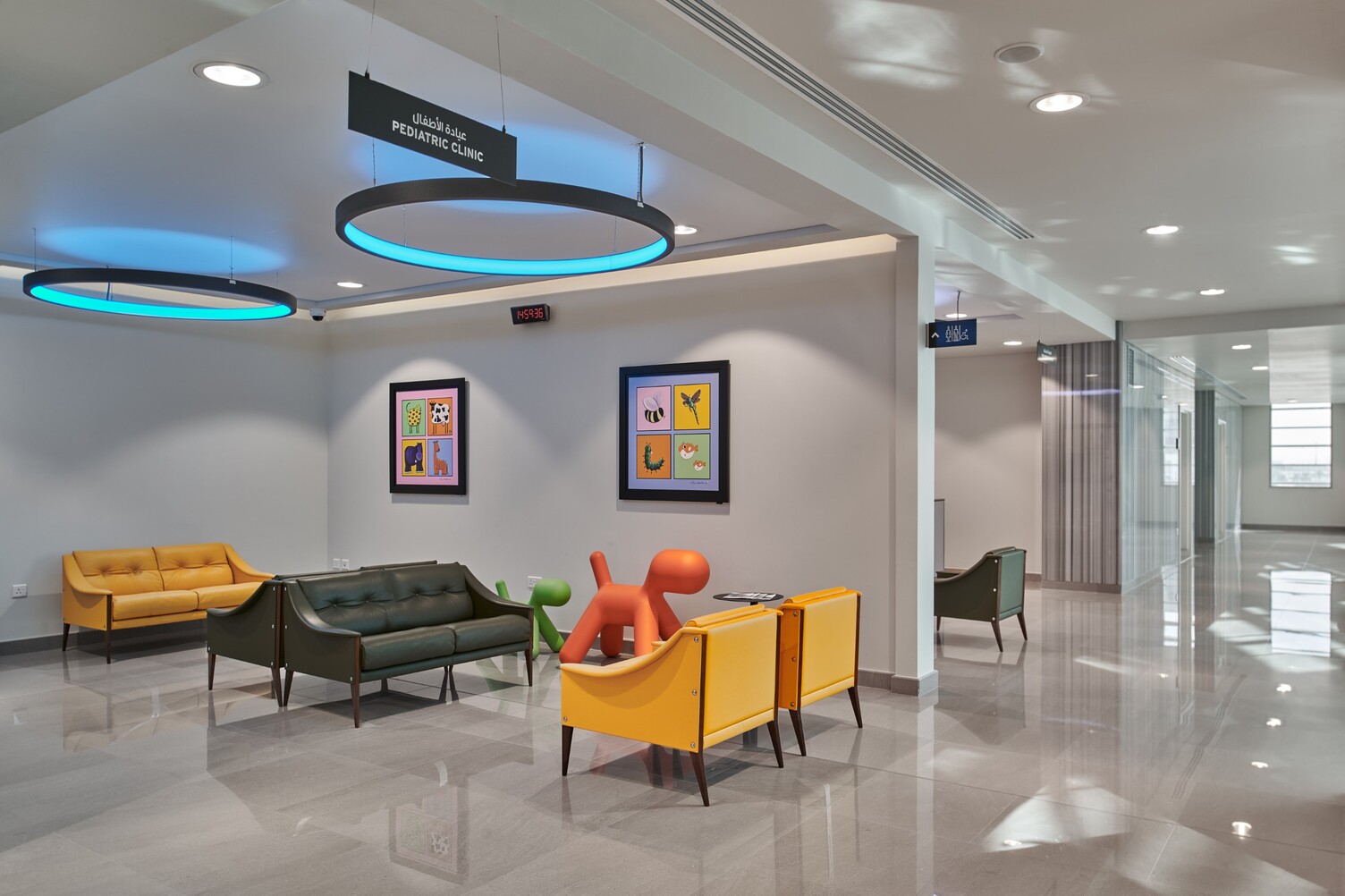 Bunt möblierter Wartebereich in einem Krankenhaus mit Kinderspielzeug an der Wand und wird von zwei großen Ringleuchten in blau beleuchtet.