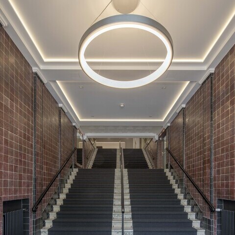 Blick auf einen Treppenaufgang mit Fokus von unten auf eine abgependelte Ringleuchte Circolo im DGB Hamburg.