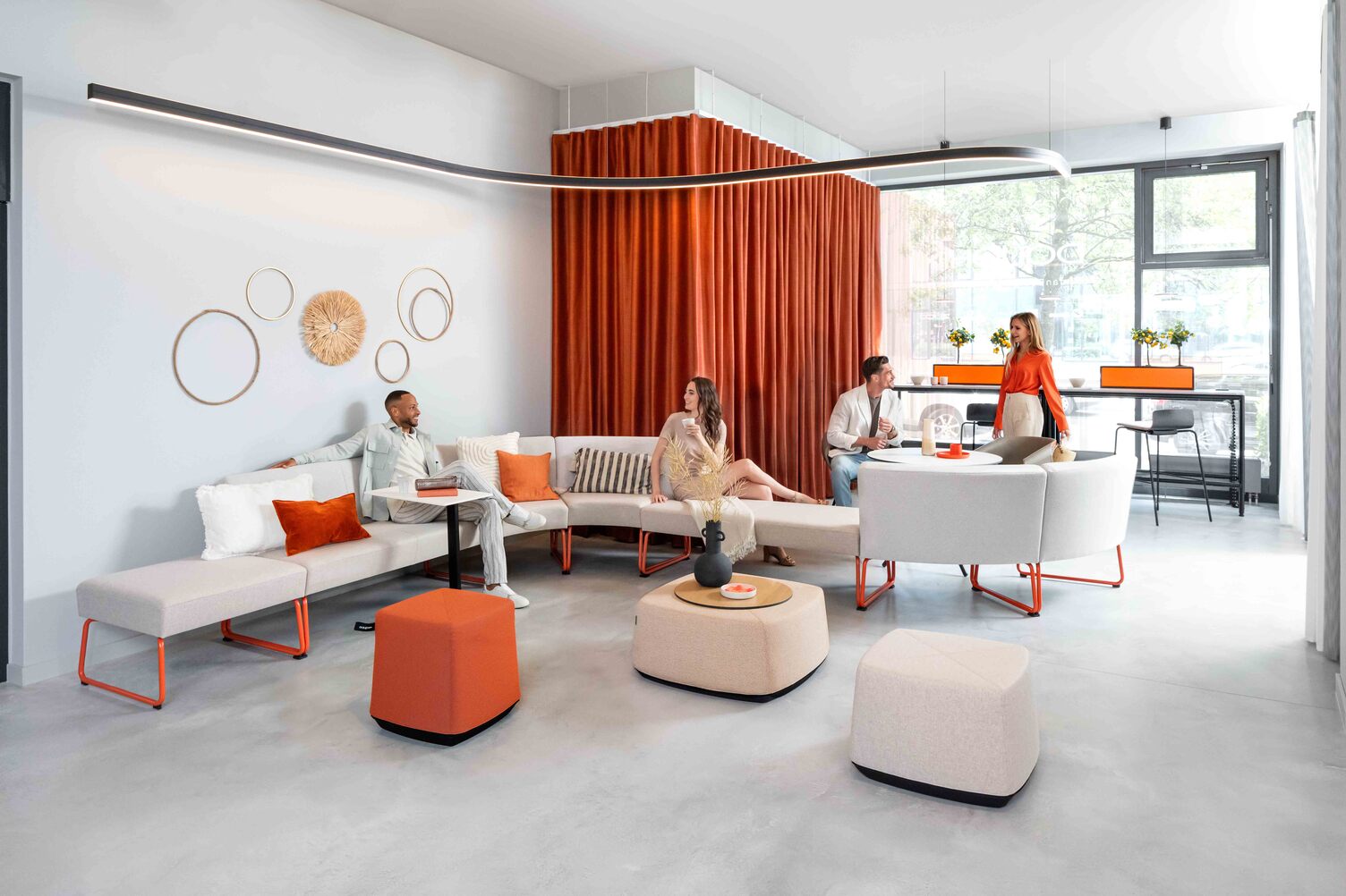 Stylish lounge area in a modern showroom with orange accents and Sattler's Duetto curved lighting fixture in Offenbach.