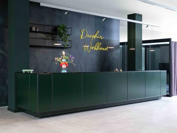 Green open reception desk of the Dauphin Workheart with Paladio System Track pendant luminaire and Paladio System LENS, each installed as a pendant version at different heights. Pendant luminaires with flat, round luminaire heads, Avveni Pendant 1, and movable Evolution Spot spotlights were also used in the Track luminaire. | © Dauphin HumanDesign® Group GmbH & Co. KG