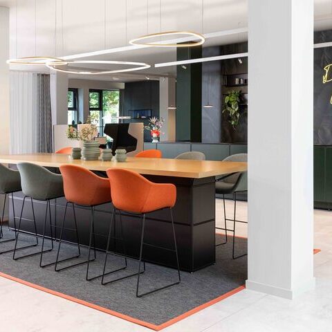 Meeting point with Slim Delta Direct luminaires from SATTLER. In the background, a reception desk with Paladio System Track luminaire and Paladio System LENS, each installed as a pendant version at different heights. Avveni Pendant 1 and Evo Spot were also used in the Track luminaire