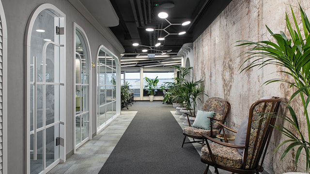 Office corridor of the dealogic office with large windows on the left and along the right-hand modern exposed concrete wall, green plants and cosy retro armchairs. Above the walkway, three white branched pendant lamps with five flat, round movable lamp heads, SATTLER AVVENI PENDANT 5, are suspended at intervals and illuminate the path. | ©  Krisztina Filep