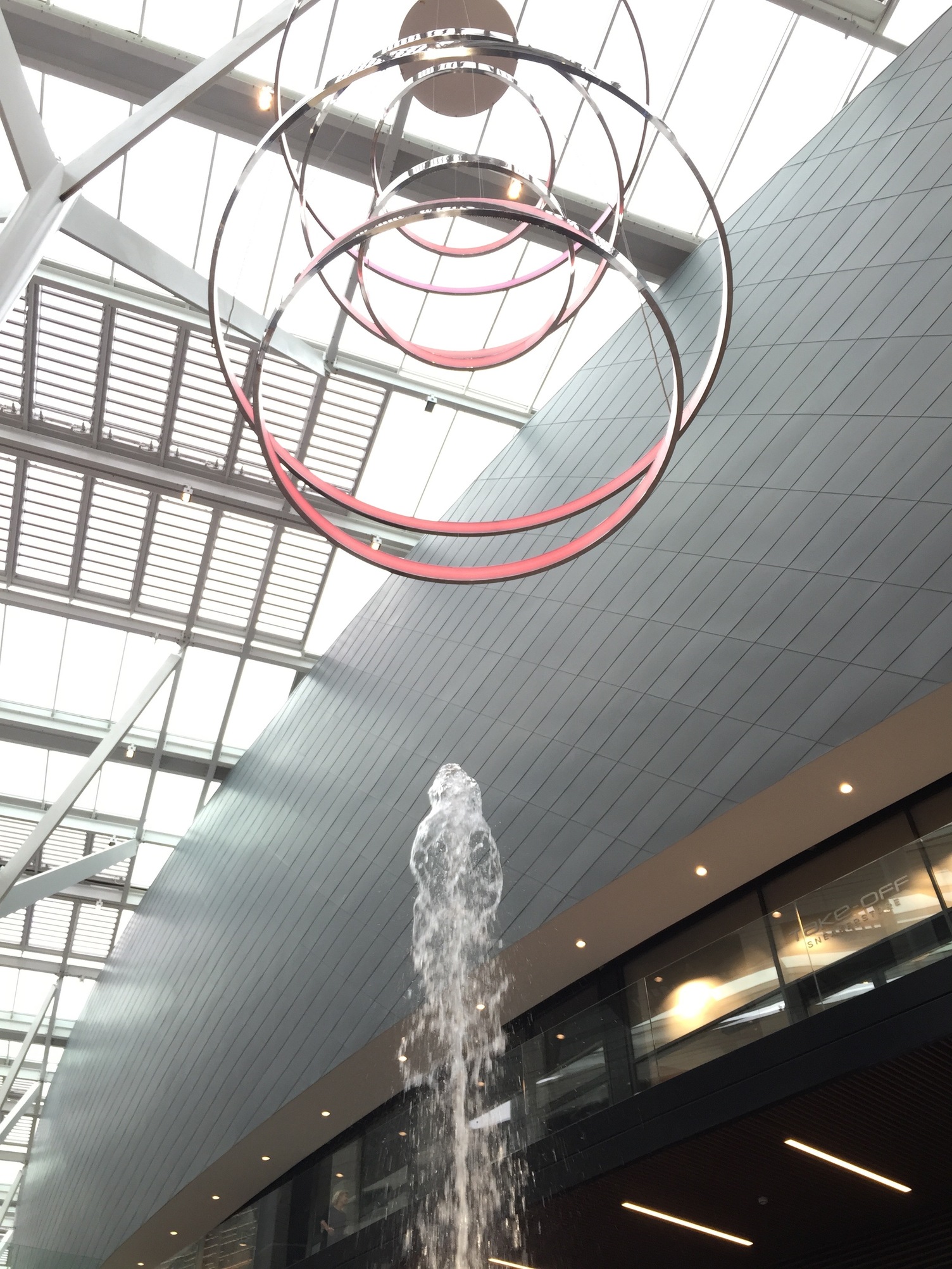 Water fountain in shopping mall, above it a light object consisting of several ring lights (CIRCOLO) on top of each other.