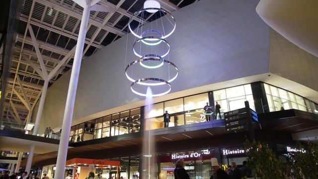 Wasserspringbrunnen in Shopping Mall, darüber eine Sonderleuchte, ein Lichtobjekt aus mehreren Ringleuchten (CIRCOLO) übereinander. 