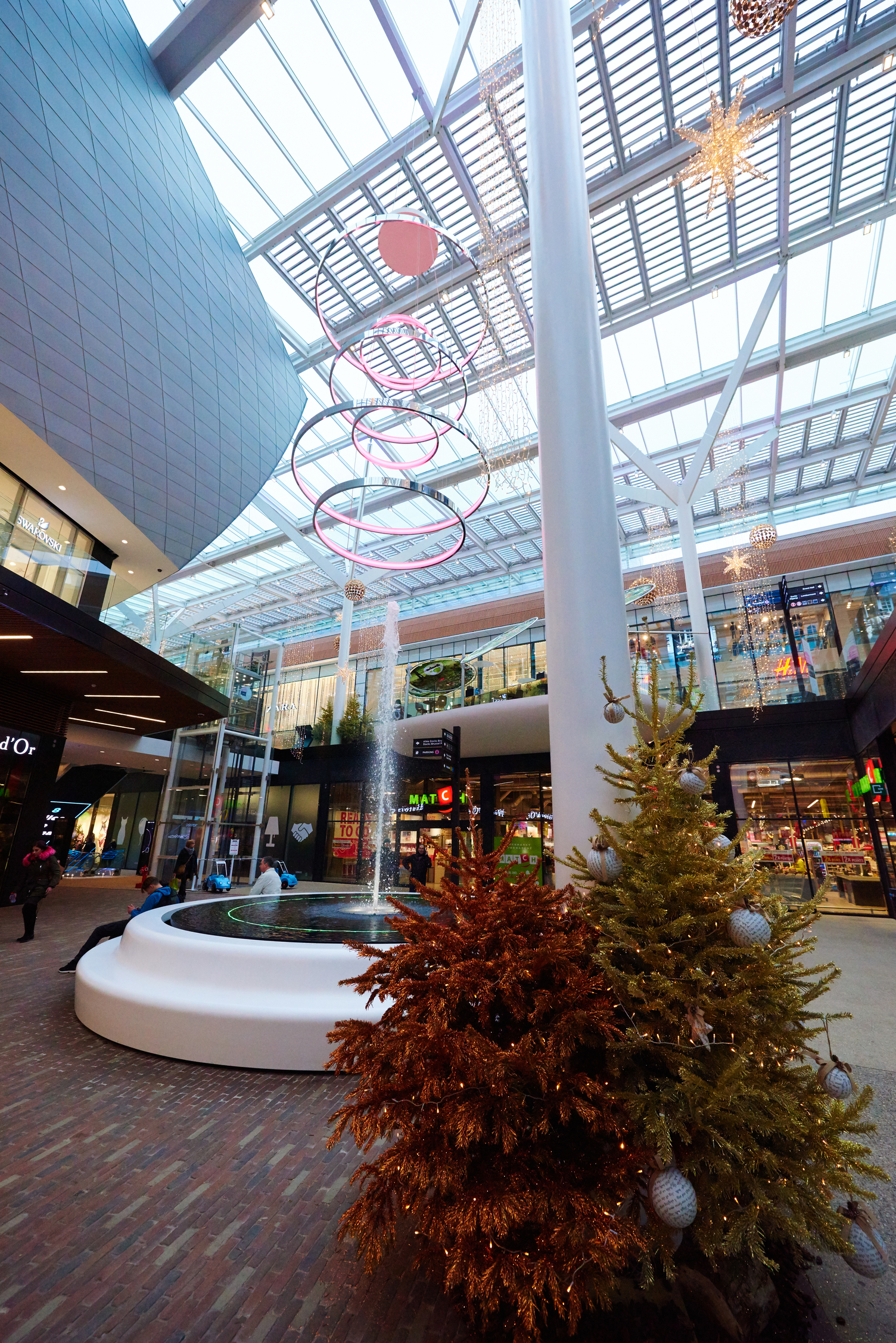Water fountain in shopping mall, above it a project luminair, a light object consisting of several ring lights (CIRCOLO) on top of each other. A Christmas tree in the front.