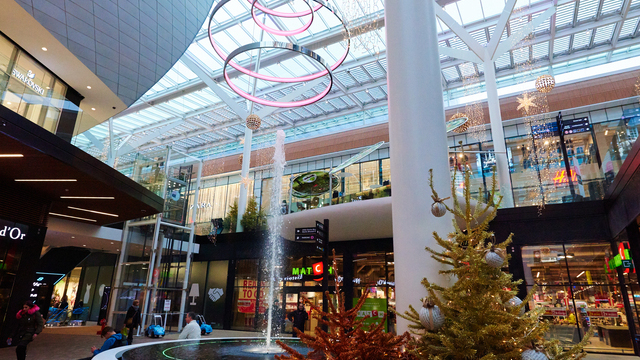 Wasserspringbrunnen in Shopping Mall, darüber eine Sonderleuchte, ein Lichtobjekt aus mehreren Ringleuchten (CIRCOLO) übereinander. Im Vordergrund ein Weihnachtsbaum. | © Yvan Glavie